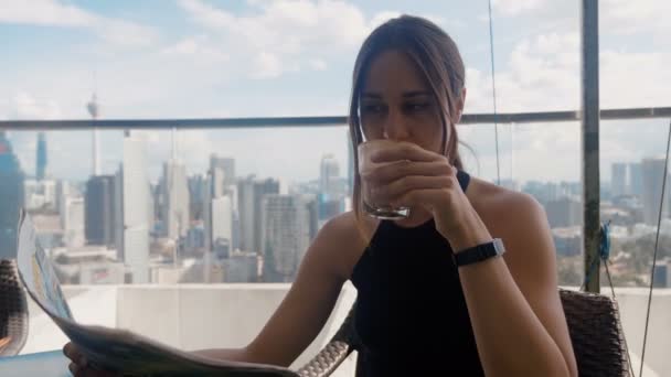 Busy businesswoman sitting in a cafe drinking latte and reading a newspaper the of skyscrapers background 4k — Stock Video