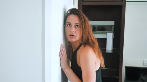 La mujer paranoica está sorprendida mirando a la mirilla. La hembra quiere esconderse de un invitado inesperado y muestra shh. 4k — Vídeo de stock