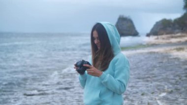DSR aynasız kamera, okyanus arka planı 4k 'de fotoğraf çeken bir kız.