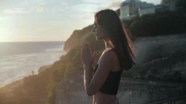 Turuncu gökyüzüne umutla bakan güzel bir kız, yakın plan. Genç bir kadının silueti okyanusun arka planında gün batımını seyrediyor..