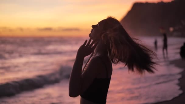 Закат над океаном. Грациозная женщина стоит на пляже и поднимает руки. 4k — стоковое видео