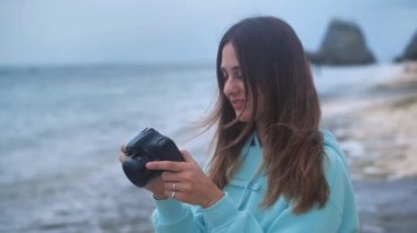 Portre hippi kadın elinde kamera olan profesyonel bir fotoğrafçı. Alacakaranlıkta okyanus arka planında fotoğraf çekiyor. 4k