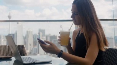 Bir iş adamı restoranda dizüstü bilgisayarında oturur, telefonu tıklatır ve meyve suyu içer.