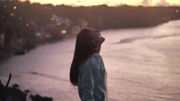 Közeli portré gyönyörű fiatal nő néz fel vizsgálja éberség elmélkedő spiritualitás a szél fúj haj élvezi a békés tengerparton naplementekor 4k — Stock videók