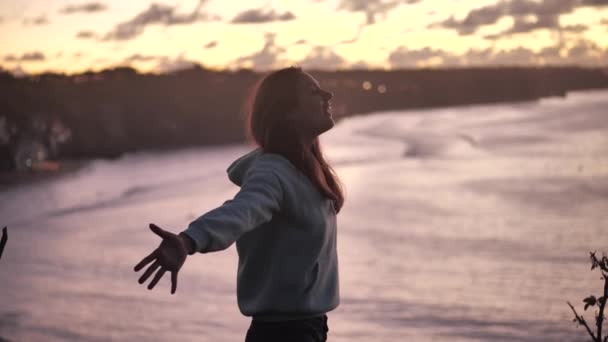 Close up retrato de bela jovem olhando para cima espalhar seus braços para os lados com o vento soprando cabelo desfrutando tranquila beira-mar ao pôr do sol 4k — Vídeo de Stock