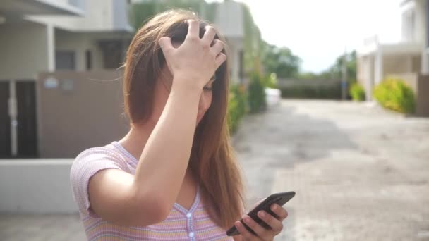 Attraente giovane donna che cammina per le strade soleggiate della città e chatta con gli amici, utilizzando il cellulare all'aperto, sfondo urbano 4k — Video Stock