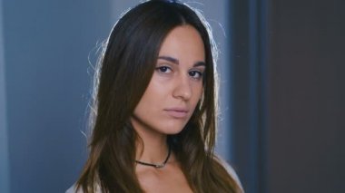 Kahverengi saçlı, büyük kahverengi gözlü, karanlık odada duran mutlu genç kadının yakın görüntüsü, kameraya doğru neşeyle gülümsüyor. Kadın portresi. 4k