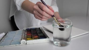 Sanatçının masaüstü. Çizmeye hazırlanırken, fırçayı suda ıslatıyor.