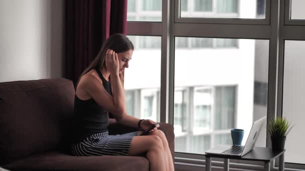 Upset young woman sitting on couch, holding smartphone in hands, received message with bad news. Stressed 20s lady thinking relations break ups after reading sms on cellphone. 4k — Stock Video