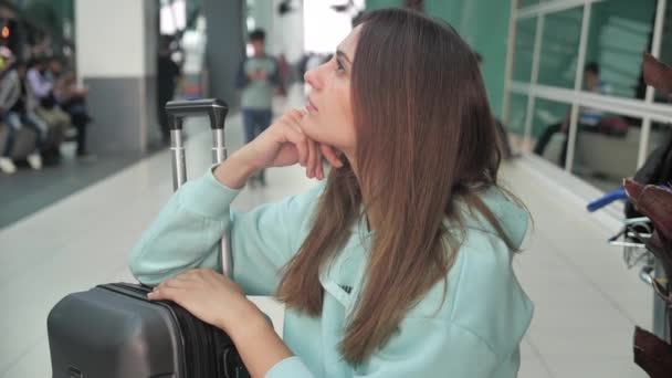 Sluit portret jonge vrouw in een luchthaven wachten op vlucht vliegtuigen. Blanke vrouw met bagage in wachtkamer 4k — Stockvideo