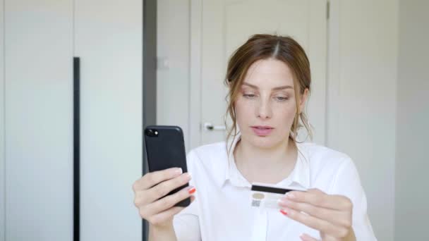 Приваблива жінка сидить вдома і робить онлайн-платежі через Інтернет з кредитної картки на своєму смартфоні. 4k — стокове відео