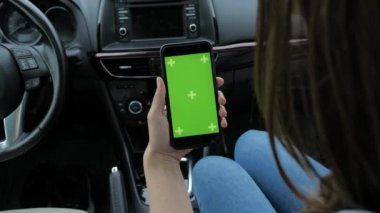 Bir kadın yeşil arka planlı bir telefon kullanıyor. Arabada oturuyor.