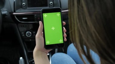 Bir kadın yeşil arka planlı bir telefon kullanıyor. Arabada oturuyor.