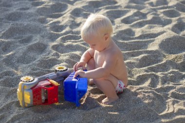 Sarışın bebek oyuncak araba ile sahilde oynarken