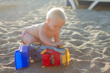 Sarışın bebek oyuncak araba ile sahilde oynarken