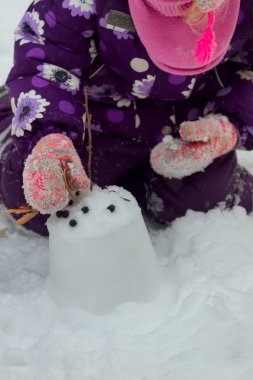 Karla oynayan, kar kalesi inşa eden ve soğuk bir kış gününde onu böğürtlen ve kuru yapraklarla süsleyen parlak renkli kar elbisesi giyen güzel bir kız. 