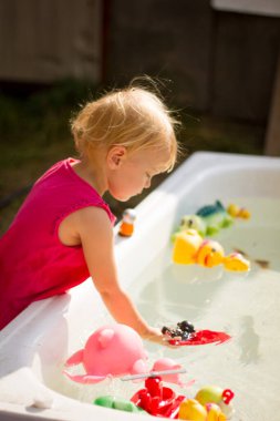 Güneşli bir yaz gününde küvette oyuncaklarla oynayan tatlı sarışın kız.