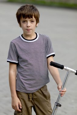 Açık havada bulutlu bir yaz gününde scooter 'ı olan yakışıklı bir genç.