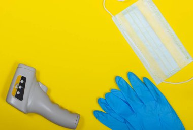 Kapalı koruma: mavi maske, lastik eldiven ve sarı arka planda termometre. Uzayı kopyala Düz yatıyordu