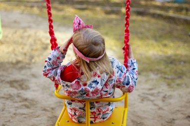 Salıncakta el yapımı kağıt taç takan sarışın kız. Arkadan Veiw