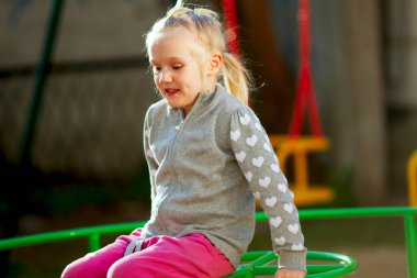 Güzel sarışın kız güneşli bahar gününde oyun bahçesinde atlıkarıncada oynuyor.