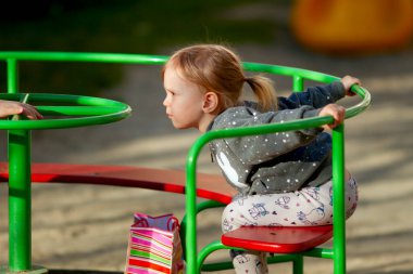 Sevimli küçük kız güneşli bahar gününde oyun bahçesinde atlıkarıncada oynuyor.