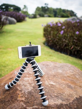 Smartphone installed on flexible tripod in garden clipart