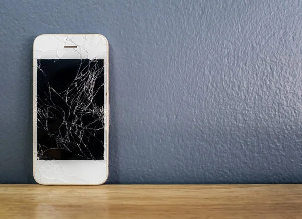Trasiga smartphone lutad mot den grå väggen — Stockfoto