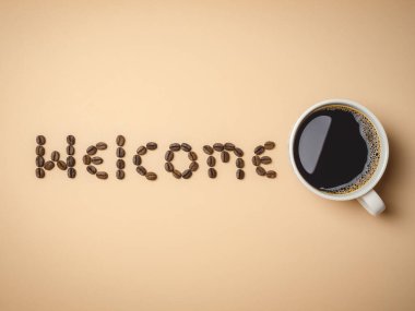 Kahve menüleri ya da kahve dükkânı tabelası için açık kahverengi arka planda, beyaz kahve fincanında sıcak kahve fincanı ve mektuplarla hazırlanmış kavrulmuş kahve çekirdekleri manzarası.