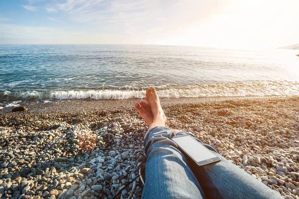 Мужские ноги на пляже с телефоном и солнечной вспышкой . — стоковое фото