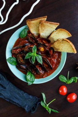 Domates soslu midyeler fesleğen ve sebzelerle servis edilen ahşap tabakta mavi bir tabakta dilimler.