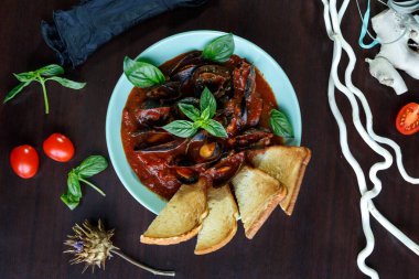 Domates soslu midyeler fesleğen ve sebzelerle servis edilen ahşap tabakta mavi bir tabakta dilimler.