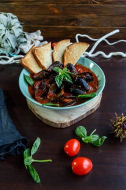 Domates soslu midyeler fesleğen ve sebzelerle servis edilen ahşap tabakta mavi bir tabakta dilimler.