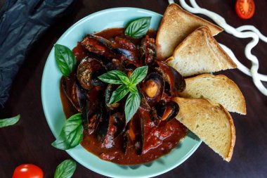 Domates soslu midyeler fesleğen ve sebzelerle servis edilen ahşap tabakta mavi bir tabakta dilimler.