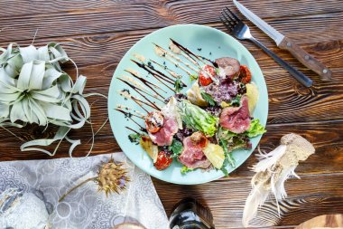 Ahşap arka planda mavi bir tabakta sebzeli ve otlu domuz eti madalyonları.