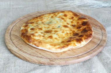   Çuval bezi arka planında ahşap mutfak tahtasında peynirli ve soğanlı Asya usulü lezzetli khachapuri tortilla.