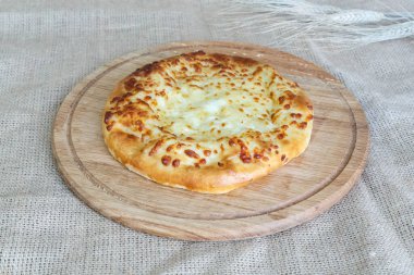   Çuval bezi arka planında ahşap mutfak tahtasında peynirli ve soğanlı Asya usulü lezzetli khachapuri tortilla.
