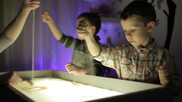 Hildren draw with their hands on the sand with illumination — Stock Video