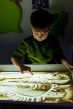 Çocuk kum kum çizer.