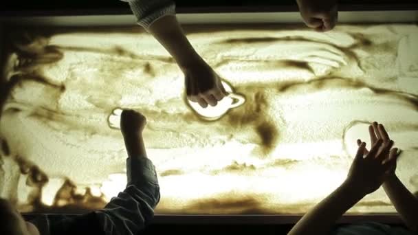 先生は 照明と砂の上を自分の手で描画する子供たちを教える — ストック動画
