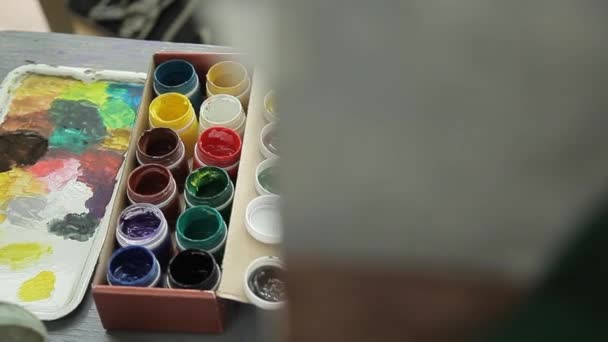 Відкриті баночки гуаші для малювання. Художник малює жовту фарбу на пензлі з політр . — стокове відео