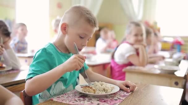 Jongen eet kotelet met een vork in de kleuterschool — Stockvideo