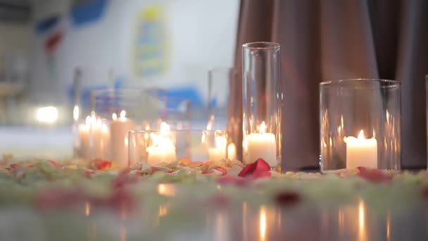 Белые горящие свечи в стеклянных колбах, лепестки роз лежат на льду — стоковое видео