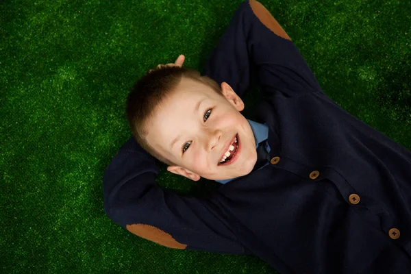 Piccolo bel ragazzo felice sorride sdraiato sulla schiena su uno sfondo verde . — Foto Stock
