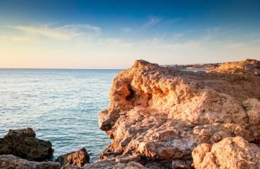 Günbatımında tropik plaj. Sahilde deniz taşları ve palmiye ağaçları