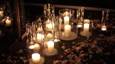 Candles in a glass flask stand on the floor with rose petals.