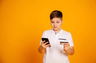 The boy pays with a credit card. boy holding a credit card and smartphone