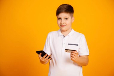 Çocuğun elinde bir kredi kartı var ve akıllı telefon satın alıyor. Mutlu genç adam internetten alışveriş yapmak için akıllı telefon ve banka kartı kullanıyor. Yakışıklı adam banka kartı ve cep telefonu tutuyor.