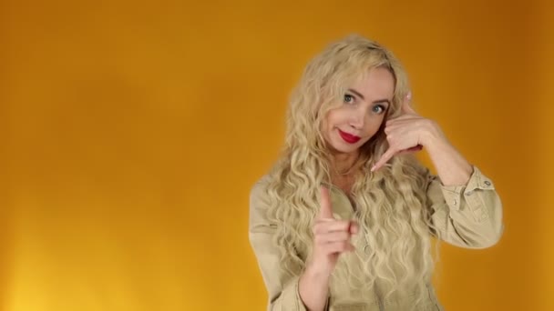 Portrait of a caucasian blonde woman smiling pointing to the camera, cheeky smiling and making a phone gesture — Stock Video