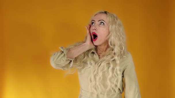 Embarrassé femme européenne blonde fronçant les sourcils autour de ses yeux, tenant sa main sur la tête avec sa bouche grande ouverte — Video